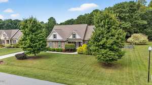 This charming single-story home at 3855 Ironwood Drive, Franklinton, features a gabled roof, brick and siding exterior, manicured shrubs, two large front yard trees, a well-kept lawn, and a driveway amid neighboring homes and mature trees.