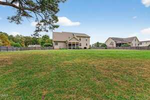 A large, grassy backyard at 3855 Ironwood Drive in Franklinton features a light brown two-story house with a covered patio; wooden fences border the yard, and neighboring houses are visible under a blue sky with scattered clouds.