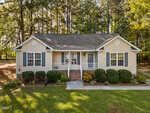 A one-story beige house with blue shutters, a front porch, white railing, and brick steps sits at 115 W Quailridge Road in Oxford. Shrubs line the front, with a sidewalk and tall trees in the background.