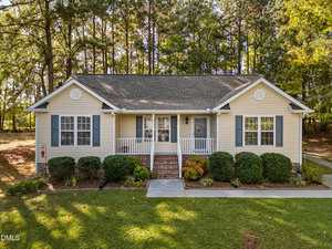 A one-story beige house with blue shutters, a front porch, white railing, and brick steps sits at 115 W Quailridge Road in Oxford. Shrubs line the front, with a sidewalk and tall trees in the background.