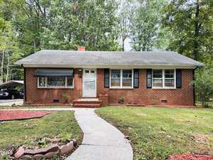 Charming single-story brick house at 906 Abbott Street, Henderson, featuring a gray shingle roof, black shutters, and a white front door. A curved concrete walkway leads to the entrance, with minimal landscaping and a carport partially visible on the left.
