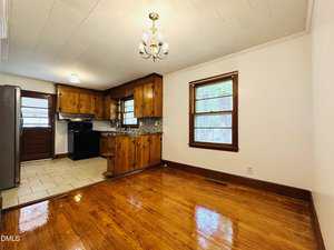 A kitchen and dining area with wooden cabinets, black appliances, a tiled floor in the kitchen, hardwood floors in the dining area, two windows, and a ceiling light fixture.