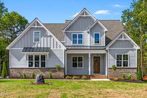 Located at 3919 Cedar Knolls Drive in Youngsville, this two-story modern farmhouse features gray siding, white trim, a brick foundation, and a covered front porch. Multiple gables and a brown front door complete the inviting curb appeal.