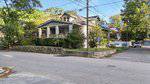 A two-story house with a covered front porch and dormer window sits on a corner lot at 1105 S Chestnut Street in Henderson. The yard features shrubs, a stone retaining wall, and faces a residential street with sidewalks in the foreground.
