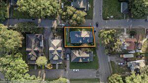 Aerial view of a residential neighborhood with several houses. One house, with a gray roof, is outlined in yellow, indicating a property boundary. Trees and streets surround the houses.