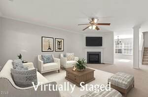 A bright living room with beige carpet, white walls, a ceiling fan, a fireplace with a TV above it, and neutral-colored furniture. The words "Virtually Staged" are overlaid at the bottom of the image.