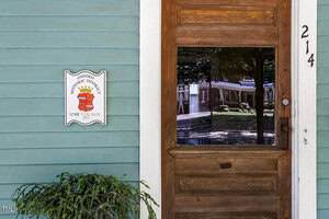 A wooden door with a glass window is set in a light blue-green wall. The number 214 is on the door frame. A sign reading "Oxford Historic District, Little-Stark House" is mounted next to the door. A plant is in the lower left.