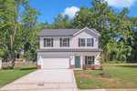 Charming two-story suburban house at 114 Hays Street, Oxford, with light gray siding, dark gray roof, attached two-car garage, and a paved driveway. The yard features green grass, small plants, and is surrounded by tall trees.