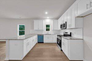 Modern kitchen with white cabinets, stainless steel appliances, light granite countertops, white subway tile backsplash, and light wood flooring. Two windows provide natural light above the sink and near the adjacent wall.