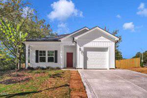 A single-story white house at 120 Clement Avenue, Oxford, with a red front door, one-car garage, and concrete driveway. The lawn is partially grassed, accented by trees and a wooden fence on the right. Blue sky with a few clouds above.