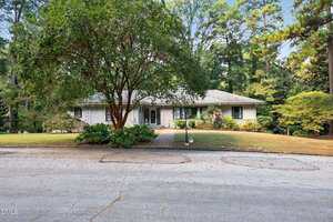 A single-story house with a light-colored exterior, two-car garage, and a large tree in the front yard sits on 910 Marrow Drive in Henderson, viewed from across a paved street and surrounded by grass and trees.
