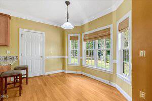 A bright breakfast nook with yellow walls, hardwood floors, three large windows with bamboo shades, a white door, two bar stools, and a pendant light hanging from the ceiling.
