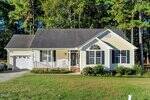 A single-story, light yellow house with white trim at 159 Waterfall Road, Henderson, features a front porch, attached one-car garage, and manicured lawn set against tall trees and dense greenery.