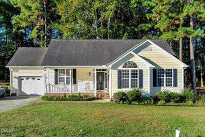 A single-story, light yellow house with white trim at 159 Waterfall Road, Henderson, features a front porch, attached one-car garage, and manicured lawn set against tall trees and dense greenery.