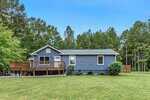 A single-story blue house with white trim sits on a grassy lawn at 4660 Dorsey Road, Oxford, featuring a wooden deck on the left side and surrounded by trees under a clear blue sky.