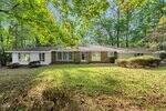 Charming single-story house at 110 Maluli Drive with stone and white siding exterior, large front windows, shingled roof, surrounded by trees and a grassy yard with scattered leaves.