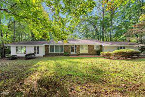 Charming single-story house at 110 Maluli Drive with stone and white siding exterior, large front windows, shingled roof, surrounded by trees and a grassy yard with scattered leaves.