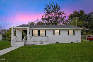 A small, single-story white brick house at 2,315 Hamilton Street, with a covered front porch, black trim around windows and door, and a neatly maintained lawn, set against a sky with purple and blue hues at sunset.