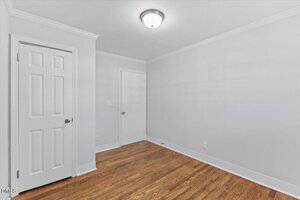 Empty room with white walls, white ceiling, and crown molding. The floor is hardwood, and there are two closed white doors on adjacent walls. A ceiling-mounted light fixture is on.