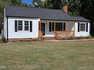 A single-story white house with black shutters and a dark roof at 1530 Oakdale Circle features a wooden front porch and steps, surrounded by a lawn with small shrubs and trees in the background.