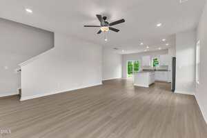 Open-concept living space with light wood flooring, white walls, a ceiling fan, recessed lighting, and a view into a modern kitchen with white cabinets, a center island, and sliding glass doors leading outside.