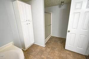 A bathroom with a white storage cabinet, a glass-enclosed shower, a partially visible bathtub, and a white door. The floor has a brown tile pattern and the walls are light-colored.