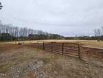 A fenced pasture with a metal gate stands in the foreground at 4173 Cannady Mill Road, bordered by bare trees on each side. Grass and exposed soil cover the ground beneath a cloudy sky, with a few cows visible in the distance.