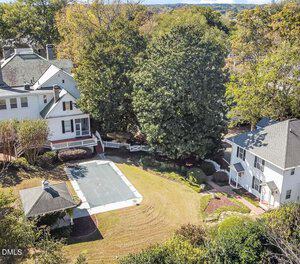 Aerial view of a residential backyard with a covered rectangular pool, a small gazebo, a large tree, and two white multi-story houses surrounded by grass, shrubs, and trees.