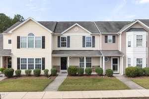 A row of two-story townhouses at 1371 Quail Circle features light-colored siding, black shutters, small covered entrances, trimmed bushes, and a sidewalk to each door. The yard is well-kept and the sky is clear.