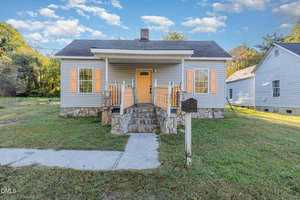 A small, single-story house at 810 Vaughan Street features beige siding, orange shutters, and a matching front door. Stone steps and a short wall lead to the entrance, with a mailbox near the walkway on the grassy yard.