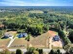 Aerial view of 3210 Bruce Garner Road, Creedmoor NC 27522 (MLS#10128691): two houses on large lots amid trees and open land, with a road in the foreground and expansive forest stretching under a clear sky.