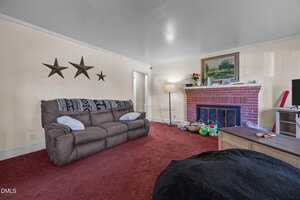 A living room with a brown sofa against a cream wall decorated with three metal stars, a brick fireplace with a painting and small items on the mantel, a bean bag, toys on the floor, and red carpet.