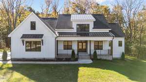 A modern white house with black trim at 1100 Waterstone Lane, Henderson, features a covered front porch, large windows, and is surrounded by grass and trees under a clear sky.