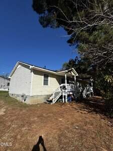 A small, single-story beige house with white trim and a covered front porch sits on a raised foundation at 911/913 Water in Henderson. Steps lead up to the porch, while a pine tree and dry ground are visible in the foreground.
