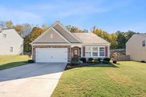A single-story suburban house at 2726 Spring Valley Drive, Creedmoor, with a two-car garage, beige siding, stone accents, and a well-maintained front lawn. The driveway and walkway lead to the front door, framed by shrubs and potted plants.