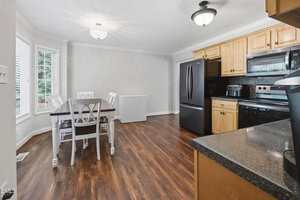 A kitchen with wood flooring, light wood cabinets, black appliances, and a black countertop. A dining table with white chairs sits near a window, and a white chest freezer is against the wall.