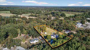 Aerial view of a rural property outlined in orange, featuring a large house, open grassy area, scattered trees, and surrounding forested land with nearby houses and roads.