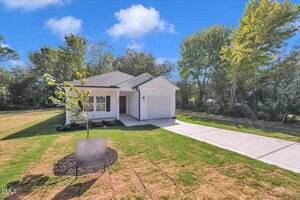 Located at 106 Summitt Avenue in Oxford, this single-story white house with a gray roof and attached garage sits on a large grassy lot with a small front tree, a concrete driveway, and is surrounded by trees under a sunny blue sky.