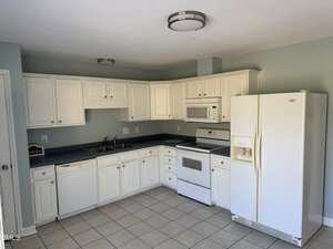 A kitchen with white cabinets, white appliances including a refrigerator, stove, dishwasher, and microwave, blue countertops, a double sink, tile flooring, and pale blue walls.