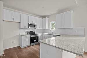 Modern kitchen with white cabinets, stainless steel appliances, white subway tile backsplash, light granite countertops, a small window over the sink, and wood flooring. The kitchen is clean and empty.