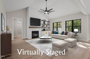 A bright, modern living room at 280 Stonewood Loop Lane, Henderson is virtually staged with a white sectional sofa, round coffee table, area rug, wall-mounted TV, fireplace, shelving, and large windows. The words "Virtually Staged" appear at the bottom.