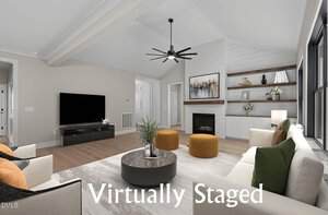 A modern living room with neutral walls, a TV on a black stand, a fireplace with artwork above, built-in shelves, two yellow ottomans, armchairs, a round coffee table, and text reading "Virtually Staged.