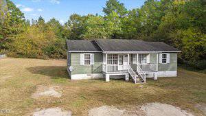 A small, single-story green house with white trim and a front porch sits on a large grassy lot at 119 Fox Pond Road in Henderson, surrounded by trees under a partly cloudy sky.