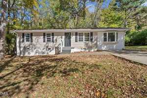 Charming single-story house at 70 Lynnbank Estates Road in Kittrell features light gray siding, white trim, a dark front door, and multiple windows. Nestled among trees, the yard is blanketed with fallen leaves and a driveway sits to the right.
