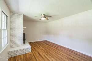 A room with a white brick fireplace and hardwood floor.