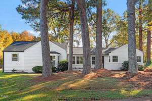 A single-story white house with black trim sits at 121 N Street in Creedmoor, surrounded by tall pine trees. The yard is covered with grass and pine needles, and the house has several windows and a gabled roof.