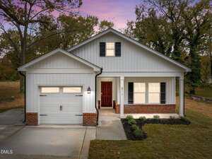 A single-story house on 511 Broad Street in Oxford features white siding, brick accents, a front porch with columns, a dark red front door, and an attached garage, set against trees and a pink and purple sunset sky.