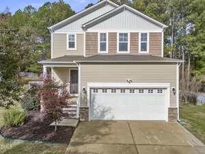Located at 1193 Shining Water Lane in Creedmoor, this two-story suburban house features beige siding, white trim, a two-car garage, a small front porch, a driveway, and landscaping with shrubs and mature trees in the background.