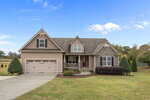 A suburban house in Wake Forest with a two-car garage, stone and siding exterior, covered front porch, and manicured lawn under a partly cloudy sky at 3522 Lavender Lane. Shrubs and trees are beautifully landscaped around the property.