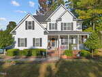 A two-story white house at 105 Torrance Court with black shutters and a covered front porch, decorated with fall items like pumpkins and a wreath. Bushes line the front, and trees stem beautifully in the background.